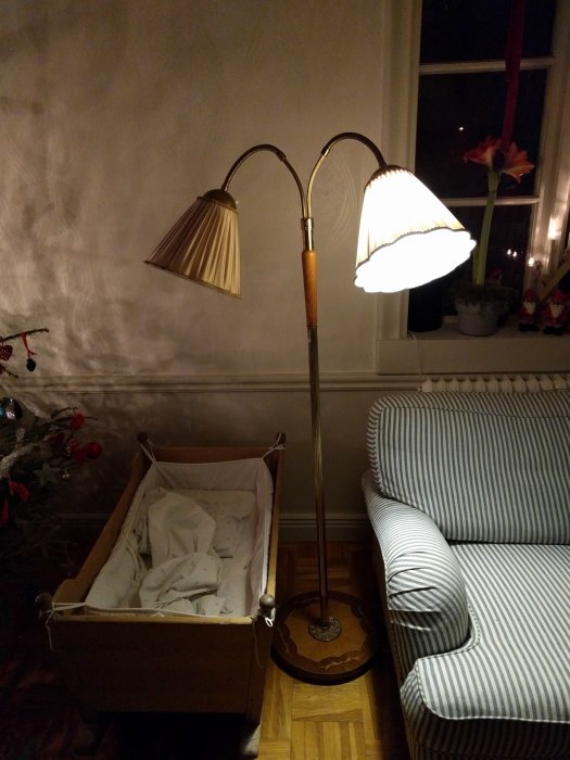 Vardagsrum med golvstående lampa, soffa, barnvagn och juldekorationer vid fönstret. Tecken på kväll eller natt.