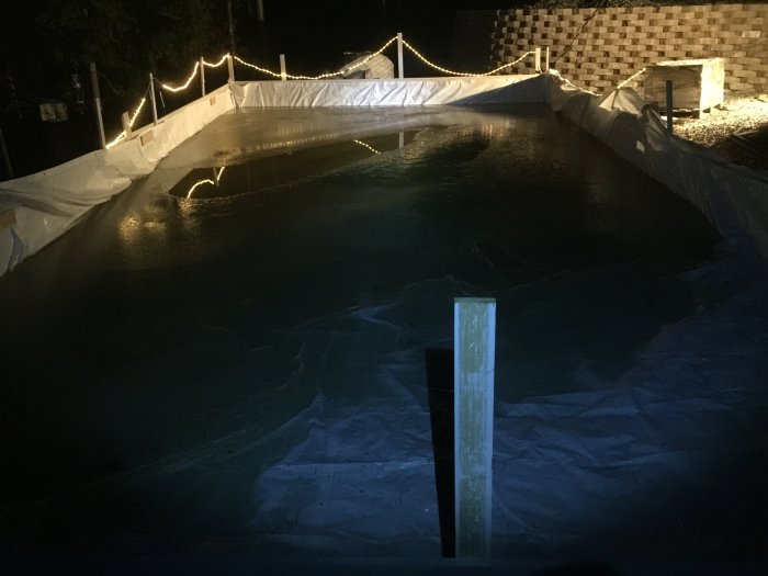 Hemmagjord isbana för hockeyspel med belysning i en trädgård på kvällen.