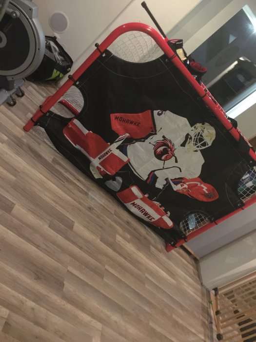 Hockeymålnät med grafik av målvakt i ett vardagsrum, används för att öva skott med puckar.