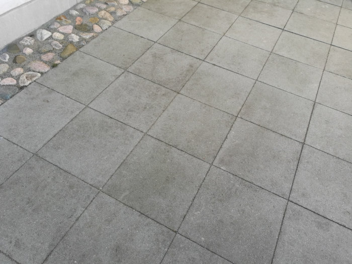 Betongplattor på en altan med synliga smutsfläckar och en kant dekorerad med stenar.