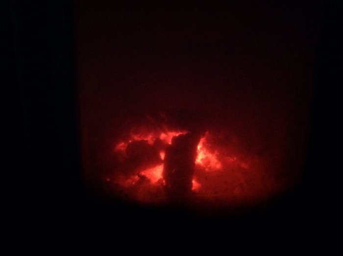 Glowing embers inside a stove visible through a dark frame, suggesting indoor heating.