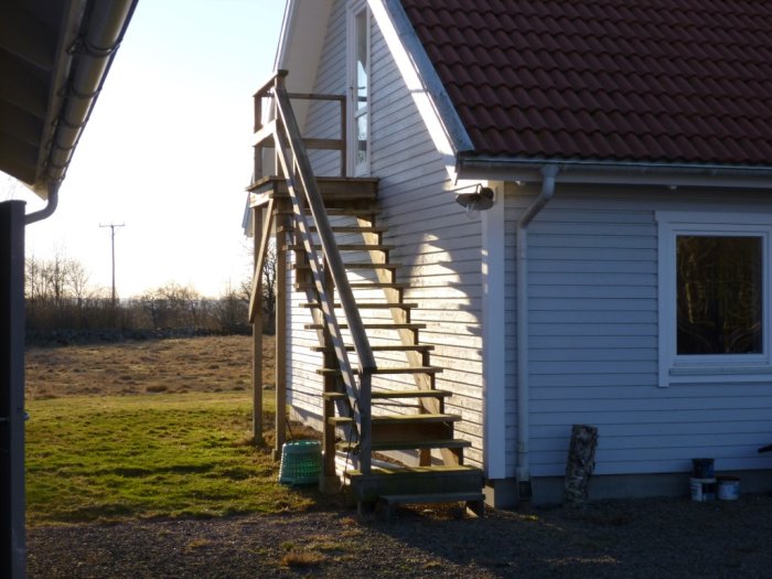 Utvändig trätrappa längs husvägg som leder till övervåning, en lösning för att undvika taklucka och stege.