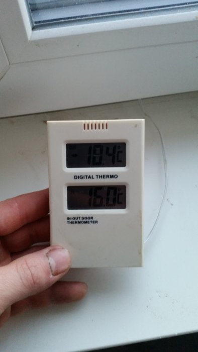 En hand håller en digital inomhus-utomhustermometer som visar 19,4 °C ute och 16,0 °C inne.