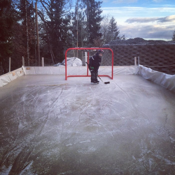 Barn i hockeyutrustning övar på hockeystopp på hemgjord isbana med skador på isen.