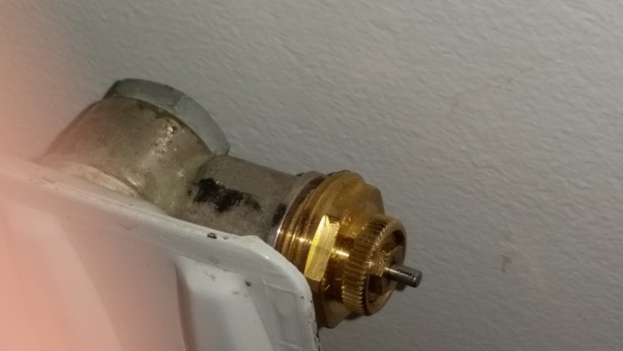 Närbild på en demonterad termostatventil på en radiator där rören syns sticka upp ur golvet.