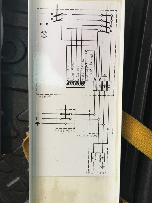 Elektriskt schema på en vit etikett som visar kopplingar för en spiskåpa, fastklistrad på en svart yta.