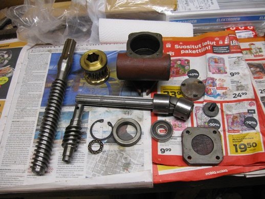 Diverse motor- och maskindelar utspridda på en tidning, inklusive axlar, lager och kopplingsplint.