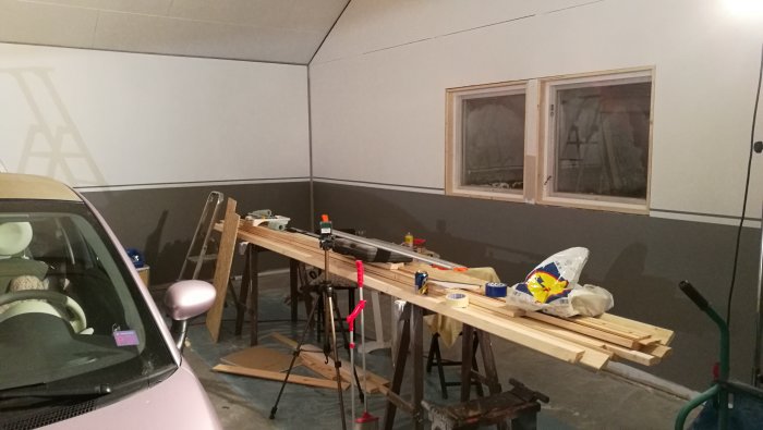 En garageinteriör med väggar målade i industrigrått och en bil, framför en arbetsbänk med byggmaterial och verktyg.