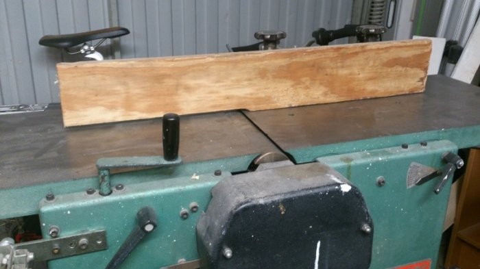 Plywoodanhåll monterat på grön hyvelmaskin med avtaget skärmskydd och synliga reglage.