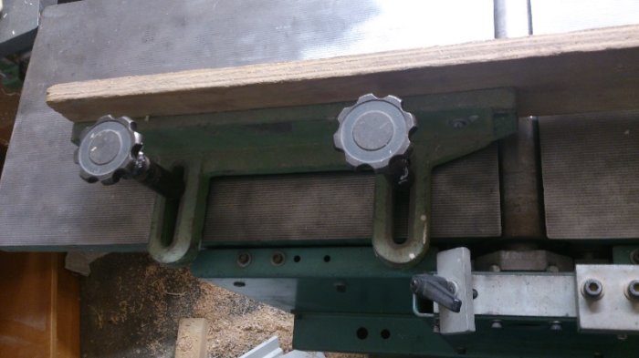 Monterat extra anhåll på trähyvelns inmatningsbord, visar avlånga hål och skruvar för justering.