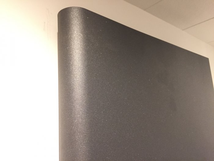 Närbild av ett vertikalt radiator-element i färgen Metal gray med glittereffekt mot en vit vägg.