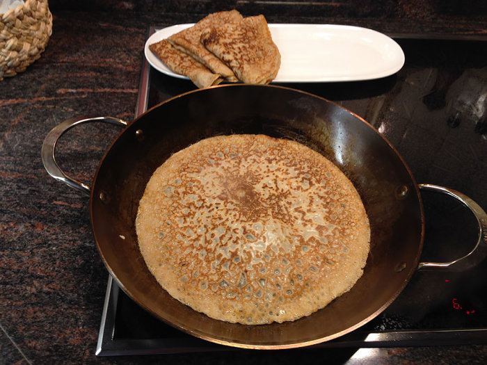 Ett pannkakslagg med en stekande pannkaka på en Husqvarna keramikhäll, intill tallrik med pannkakor.