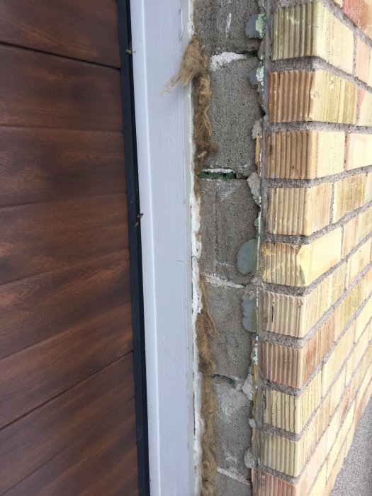 Nymonterad brun garageport i anslutning till tegelvägg, med synlig gammal fogsprängning och isoleringsmaterial.