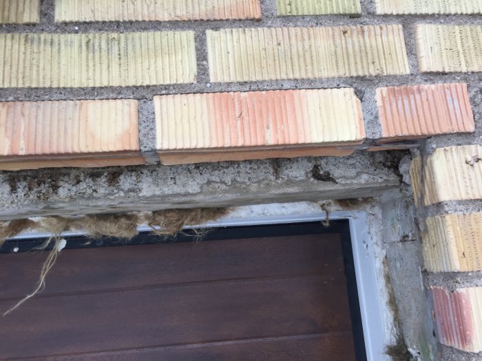 Delvis exponerat tegel och möjligt isoleringsmaterial ovanför en nyinstallerad garageport.