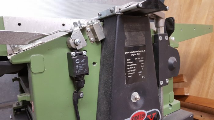 Närbild av en gröns målad stålmaskin med tekniska specifikationer och säkerhetsmärkningar.