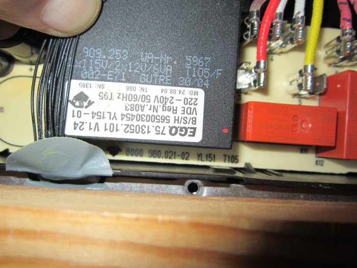 Öppen elektronisk apparat med ledningar och en röd transformator med specifikationsetikett.