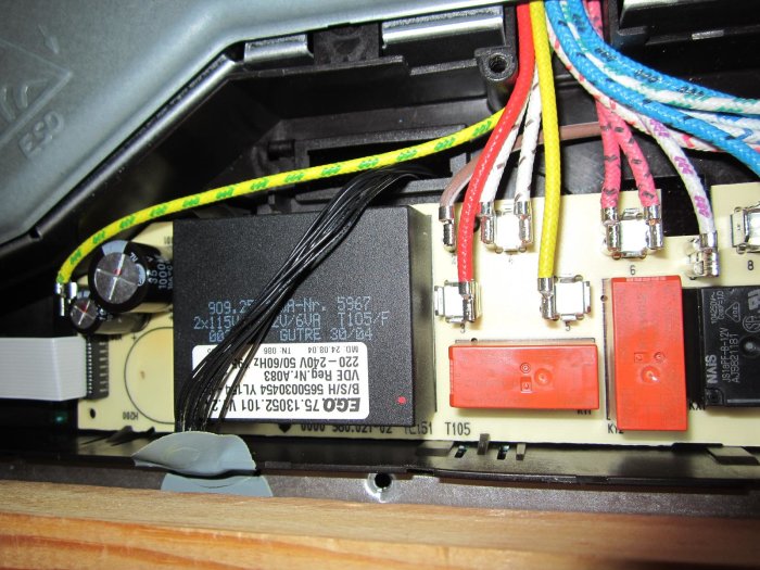 Elektronisk kretskort med transformator, reläer och tätt liggande svarta sladdar i en apparat.