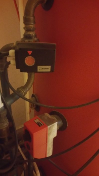 Bild av en Wamsler-röd braskamin med synlig pump och rörinstallation.