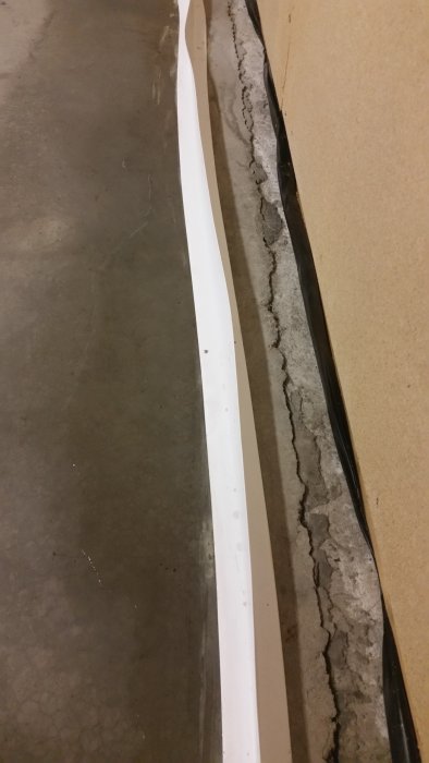 Golvlist liggande på betonggolv bredvid en vägg, indikerar ett pågående byggprojekt.