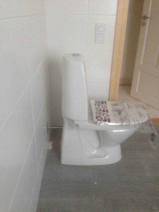 Nytt toalettstol i badrum med öppen avloppsrör sticker ut från väggen.