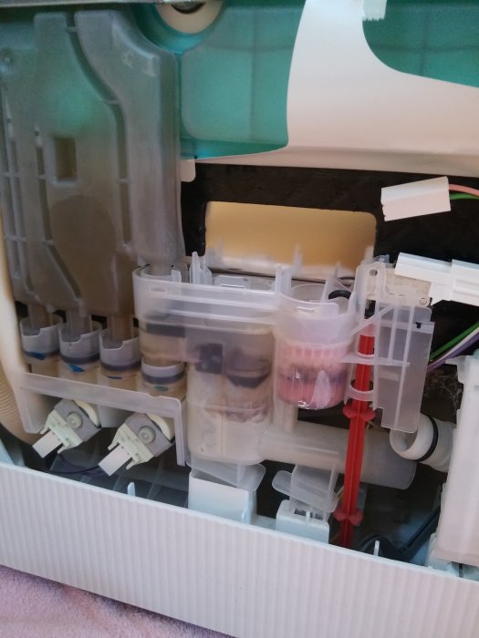 Interiör av en maskin med en röd flottör, kablar och genomskinliga behållare, delvis demonterad.