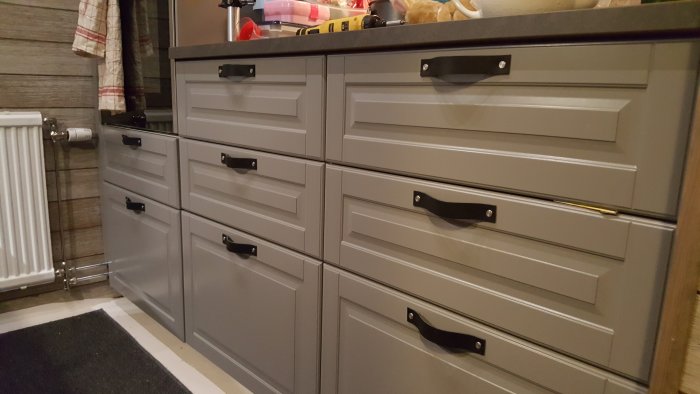 Gråa kökslådor med nya svarta handtag installerade, resultat av renovering.