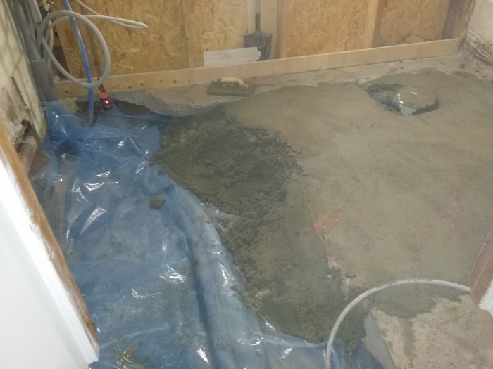 Nyutgjuten betong i ett rum med synliga plastsäckar och verktyg på skyddsplast.