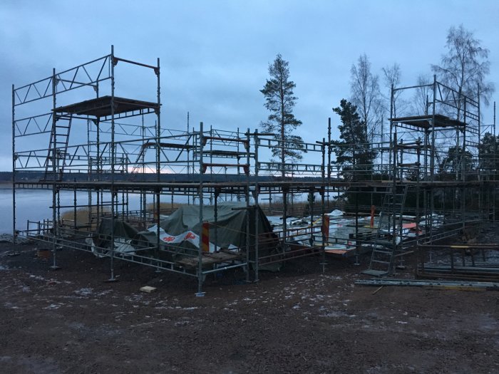 Byggnadsställningar vid en husgrund nära en sjö, i skymningen, redo för husleverans.
