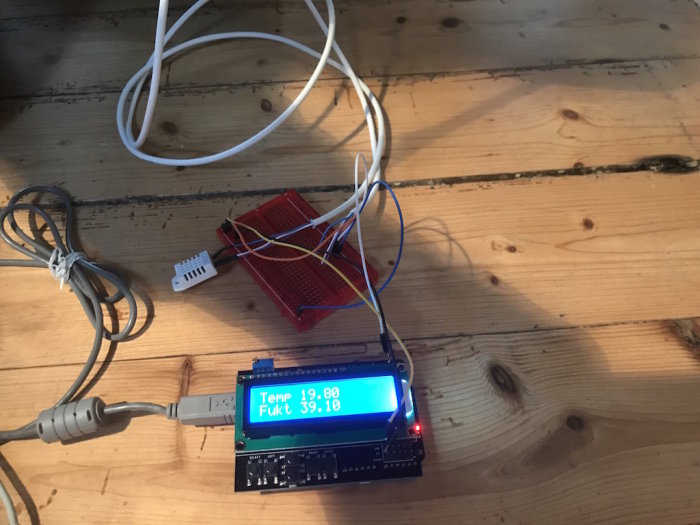 Elektronikprojekt med Arduino Uno och LCD-skärm som visar temperatur och fuktighet på träbord.