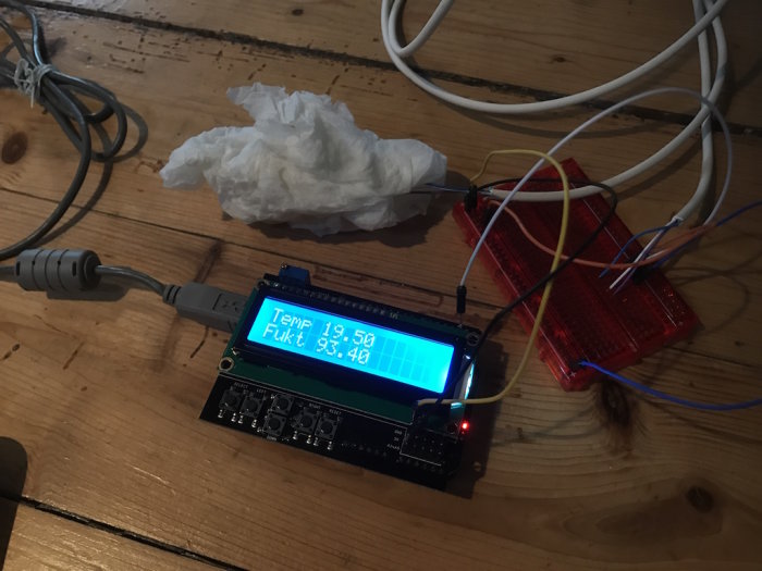 Arduino Uno kopplad till LCD-skärm och sensor omgiven av fuktigt hushållspapper på träbord.