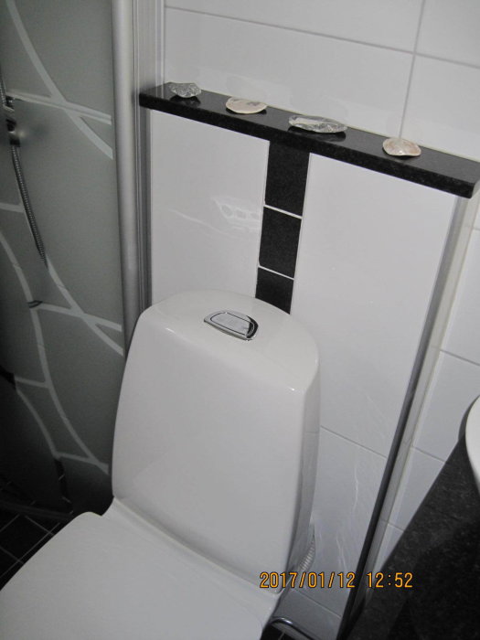 Toalett i hörnet av ett badrum med en utbyggnad bakom för att dölja avloppsröret.