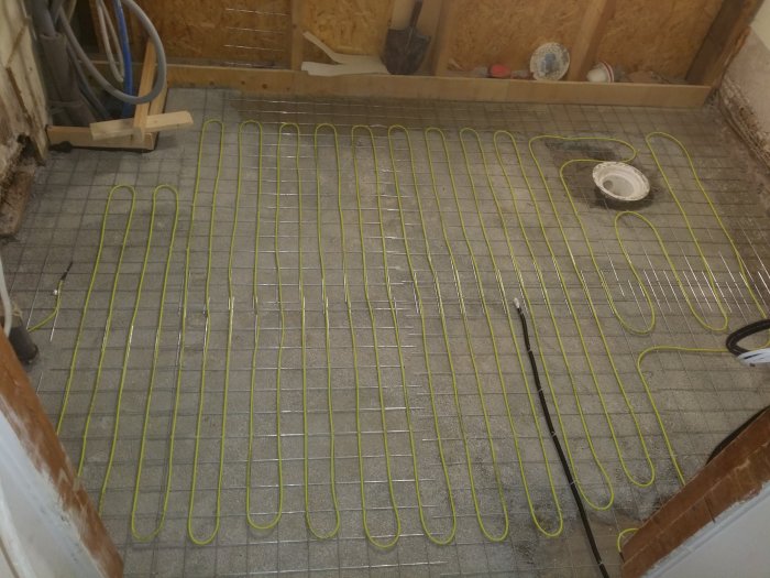 Armeringsnät med gul golvvärmeslinga utlagd i en betonggrund under förberedelse för spackling.