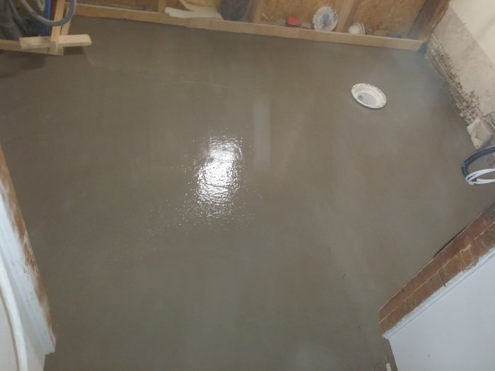 Nyligen pågjuten fallspackling på ett betonggolv med synlig brunnsring och kabelslangar vid väggen.