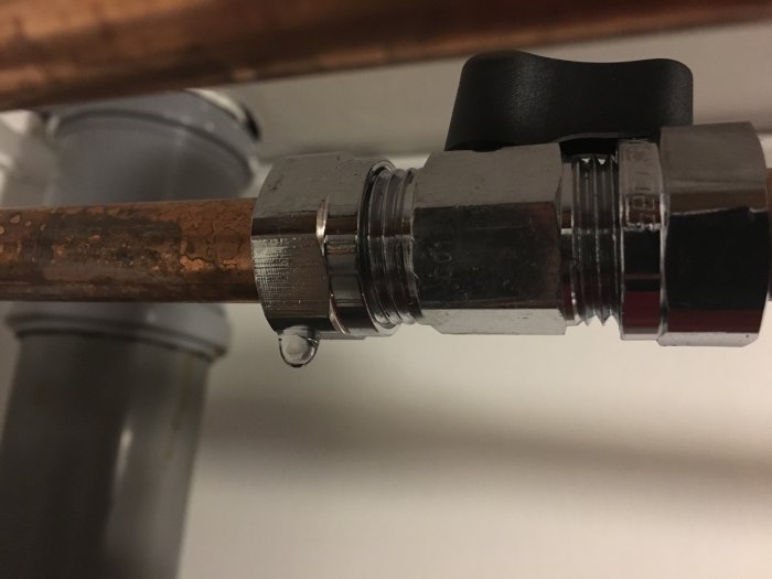 Koppling mellan kopparrör och svart ventil läcker med en vattendroppe som syns.