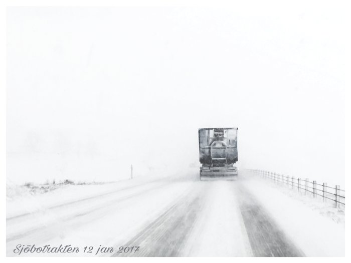 Lastbil på snöig väg under stormbyar med dålig sikt och fallande snö.