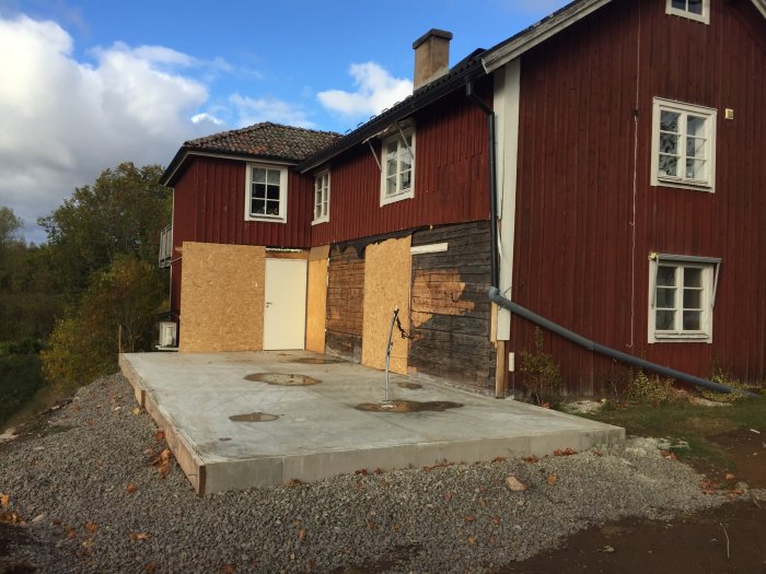 Röd trävilla under renovering med avtäckta väggar och nygjuten betongplatta.