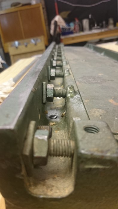 Närbild av underredet på en maskin med justerbart mekanism och skruvar som visar slitage och korrosion.