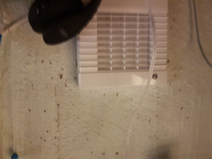 Ventil för tilluft installerad på kontorets vägg med synliga kablar.