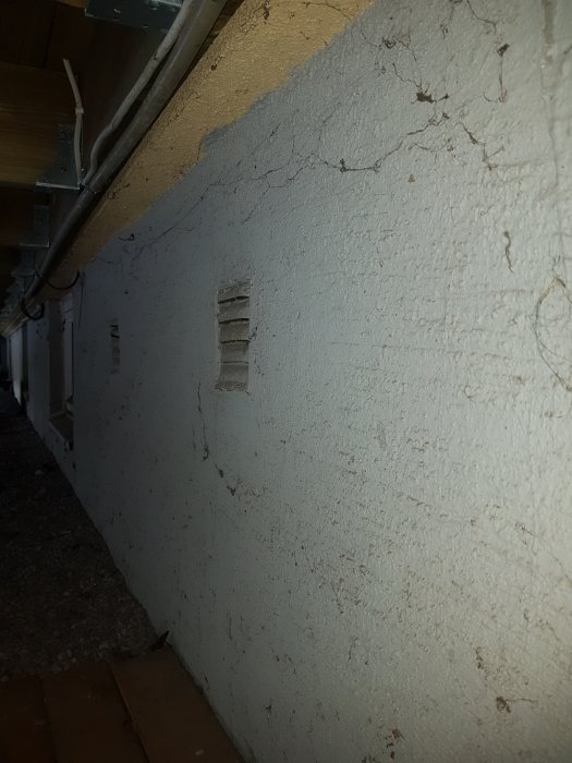 Ventilationsgaller på en sprucken och flagande vägg utomhus vid dagsljus.