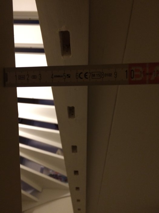 Trappstolpe med tomma spår och hål för spaljéribbor, mätsticka visar måtten för att skapa nya ribbor.