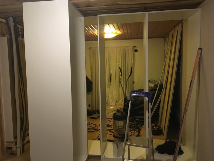 Nybyggda vita garderober med öppna dörrar och rördragning i bakgrunden.