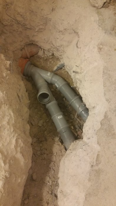 Nyinstallerade gråa avloppsrör i ett grävt schakt i marken.