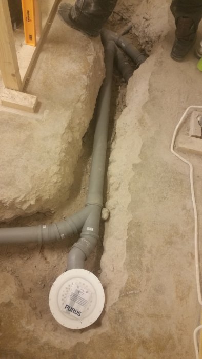 Nylagda avloppsrör i grått med etikettmärkt Purus-inspektionslucka i betonggolv under renovering.