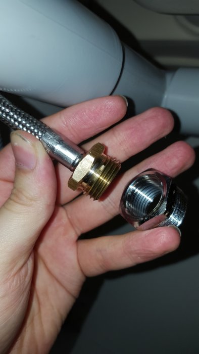 Hand håller en ej monterad koppling med en vattenslang och gängade metallbackar.