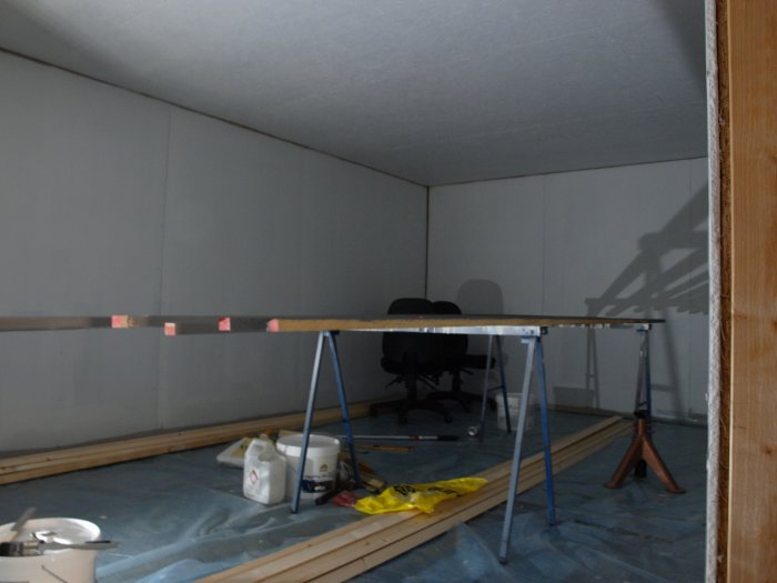 Pågående arbetsplats i rum under renovering med lister, målfärg och verktyg på golvet.