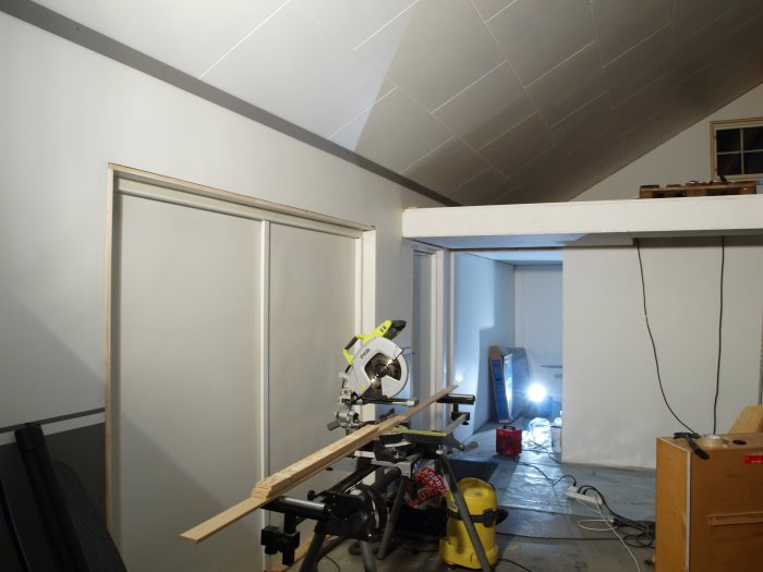 Renoveringsarbete med nyinstallerade taklister och målat tak i ett rum med byggverktyg.