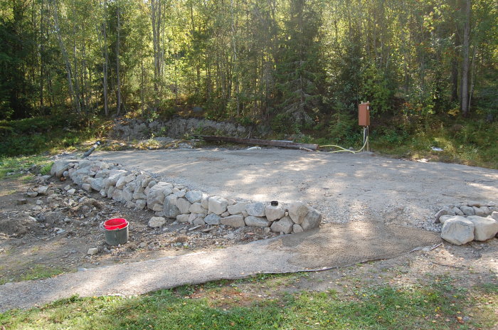 Grusplan med stödmur av sten och elskåp förberett för carportbyggnation.