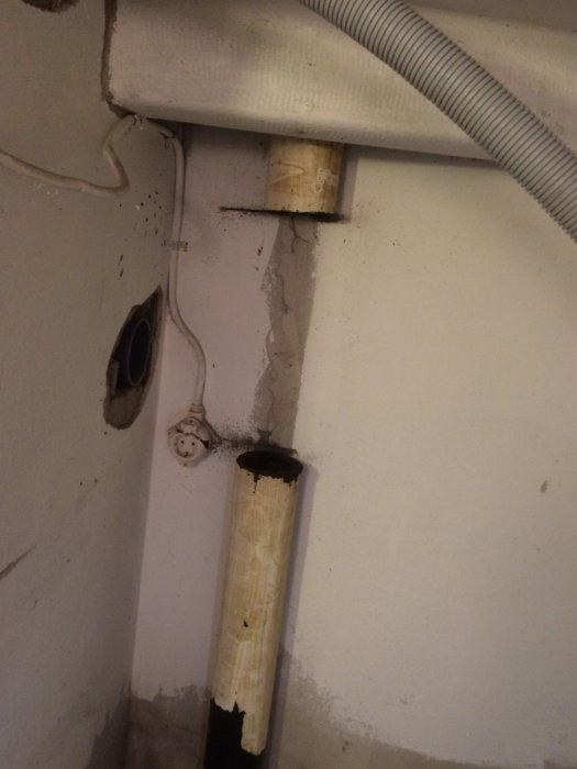 En ofullständig installation av avloppsrör i källare, med synliga rörstumpar och ledningar intill en spröd vägg.