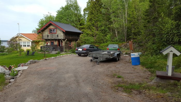 Uppfart med bilar och släpvagn framför hus med planerad bergssprängning i bakgrunden.