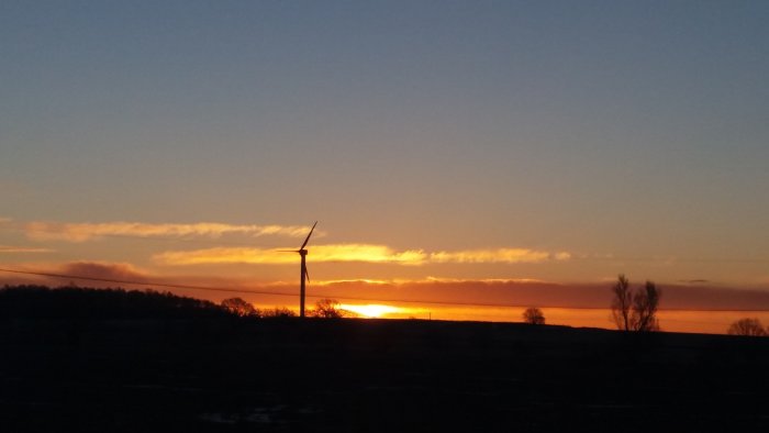 Soluppgång med silhuett av vindkraftverk mot en orange himmel.